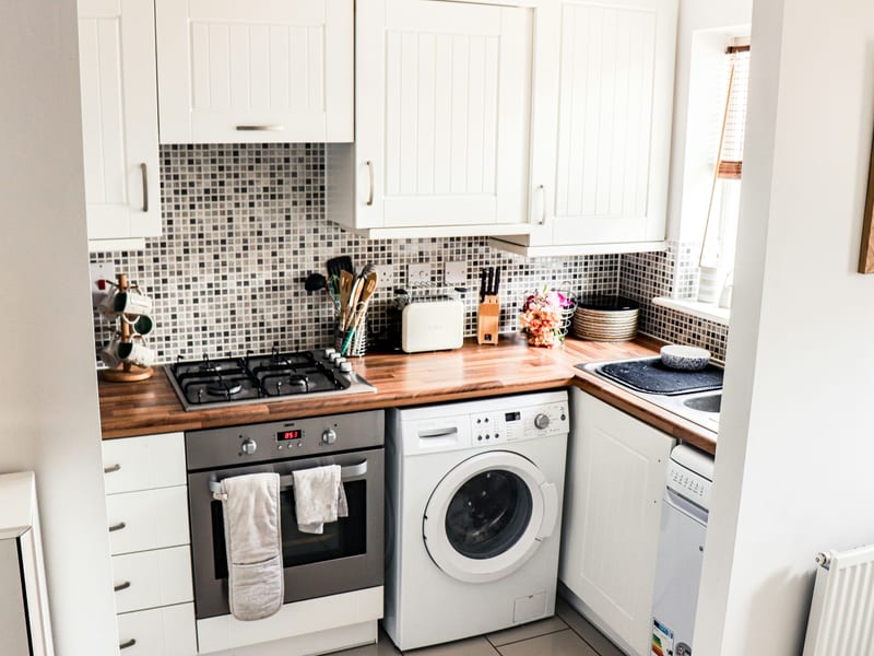 A white front-loading washing machine installed under a kitchen counter next to a built-in oven